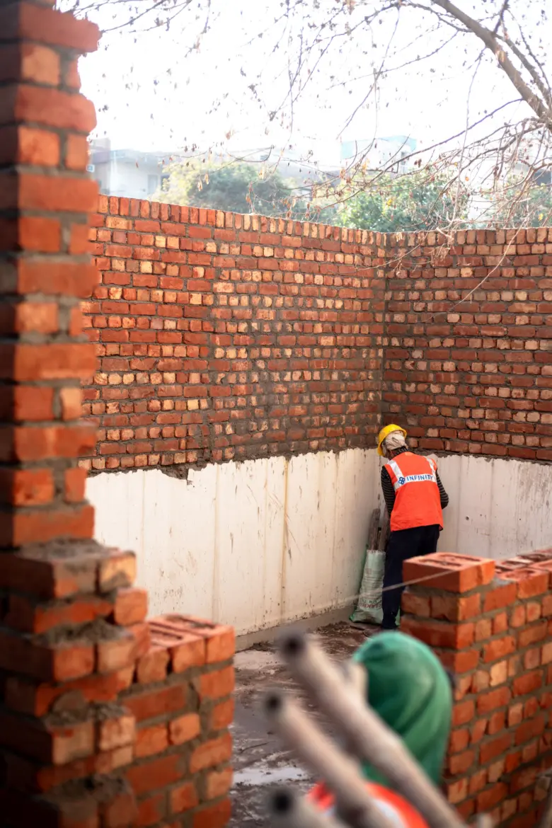 Stavebník staví cihlovou opěrnou zeď s tvarem.