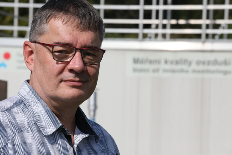Muž v brýlích před budovou s informacemi o kvalitě ovzduší.