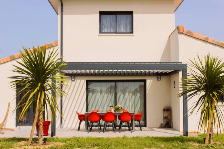 Hotová pergola před domem s červenými židlemi.