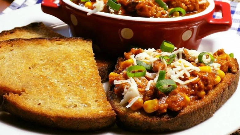 Topinka s chilli, kukuřicí, sýrem a cibulkou na bílém talíři.