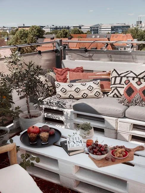 Uspořádaný malý balkon s paletovou nábytkem a dekorací.