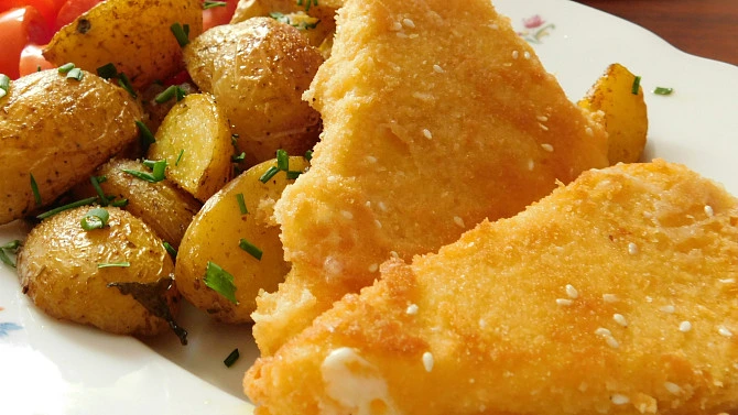 Zlatě opečený smažák s bramborami na bílém talíři.