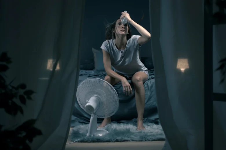 Žena v noci potí se na posteli s ventilátorem.