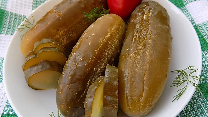 Naložené okurky na talíři s petrželkou vedle červené rajčete.