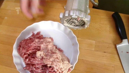 Mleté hovězí maso s ručním mlýnkem na dřevěném povrchu.