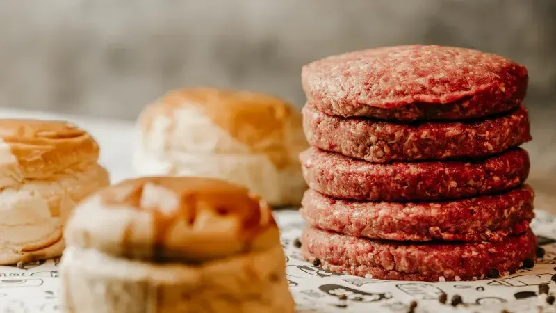 Surové hovězí placky pro burgery s chlebovými rohlíky.