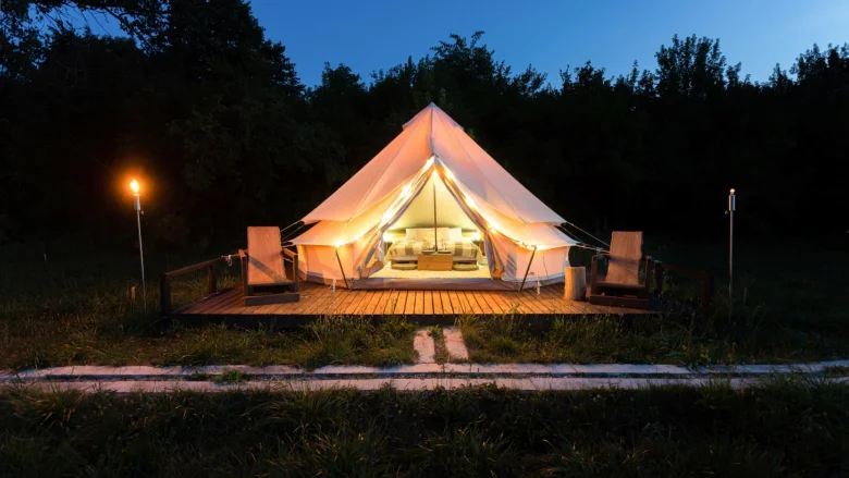 Luxusní glamping stan na dřevěné terase za soumraku.