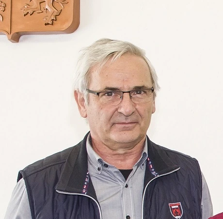Portrét středověkého muže s brýlemi před bílou stěnou.