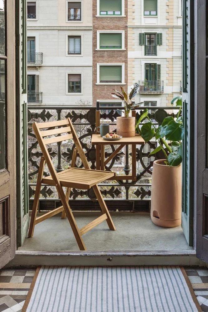 Malý balkon s dřevěnou židlí, stolem a rostlinami.