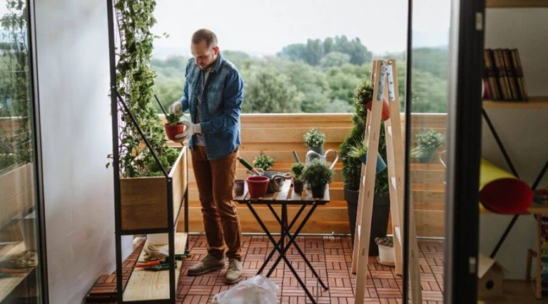 Muž upravuje rostliny na malém balkóně s nářadím.