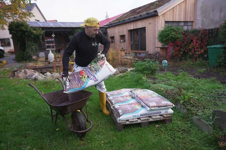 Muž přelévá zeminu do vozíku v zahradě.