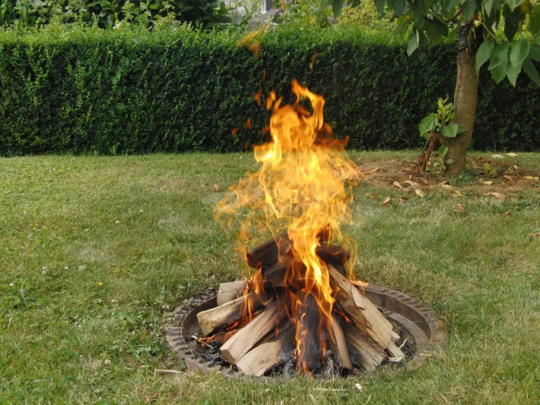 Hořící oheň v kovovém ohništi na trávníku.