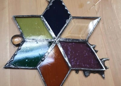 Rukou vyrobená vitráž ve tvaru hvězdy s barevnými skleněnými panely.