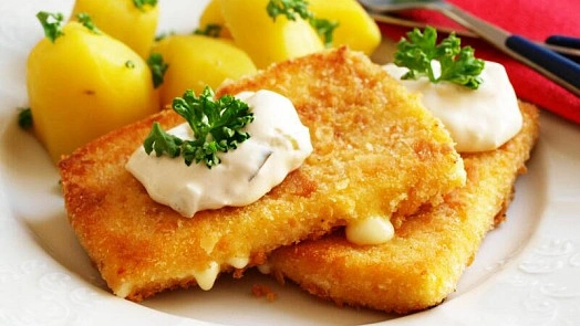 Zlatě opečený smažák s bílým omáčkou a bramborami.