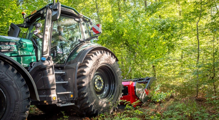 Zelený traktor pracuje v lese jako součást zemědělské činnosti.