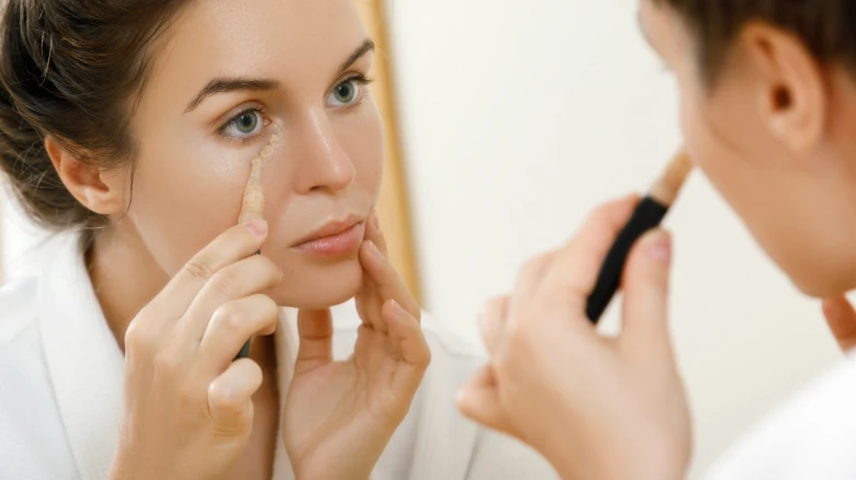 Žena aplikuje make-up na stařecké skvrny před zrcadlem.