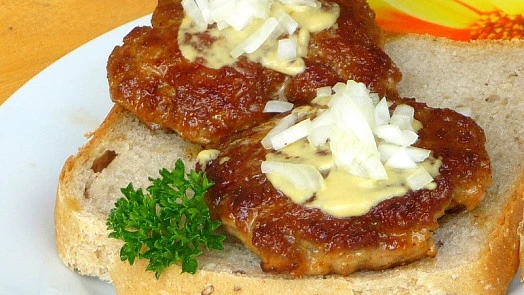 Dva smažené vepřové řízečky na chlebu s hořčicí a cibulí.