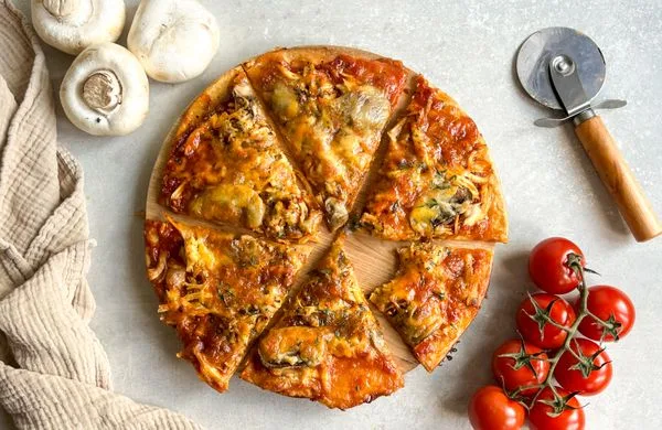 Připravená pizzu s žampiony na dřevěném prkénku.