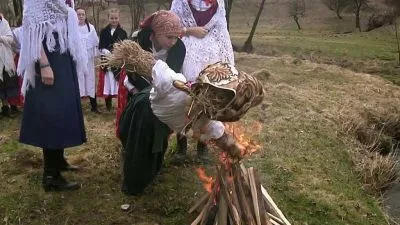 Lidé v tradičních kostýmech hrají u velikonočního ohně s rituálními předměty.